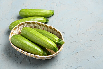 Wicker bowl with many fresh green zucchini on blue background