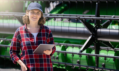 Woman farmer with digital tablet on a background of harvester. Smart farming concept