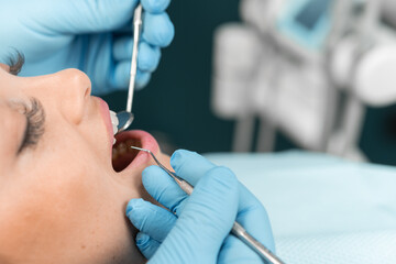 In the dental chair, the patient watches with interest the dentist, who improves her smile. The doctor displays a high level of professionalism and focus on every detail. - obrazy, fototapety, plakaty