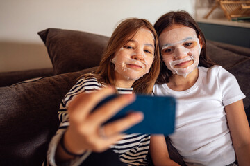 Two pretty teenage girls with disposable fabric moisturizing beauty masks on their faces take a...