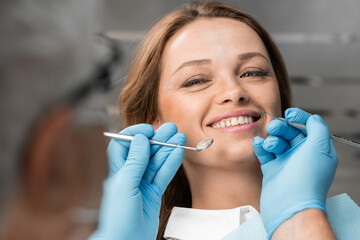 The patient, sitting in dental chair, proudly demonstrates her clean and healthy smile. A dentist...