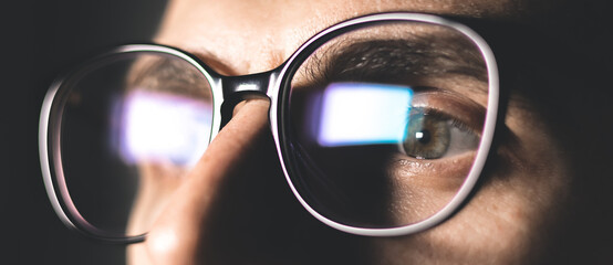 Man works on internet. Reflection at the glasses from laptop..Close up of man's eyes with black female glasses for working at a computer. Eye protection from blue light and rays.