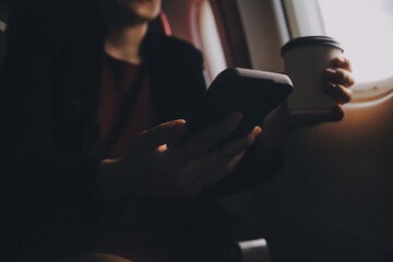 Blonde female tourist checking incoming notification on smartphone sitting on seat of airplane with netbook.Young businesswoman share media from telephone on laptop computer during plane flight