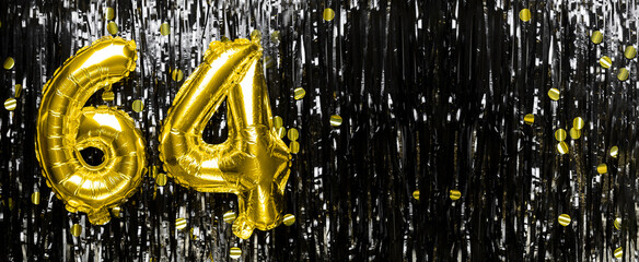 Gold foil balloon number number 64 on a background of black tinsel decoration. Birthday greeting...