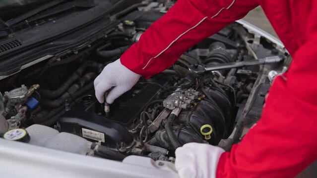 Car mechanic changes spark plugs in a car engine. Installs a new iridium spark plug into the spark plug well.