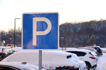 Parking space road sign on cars background. Snow weather in winter city