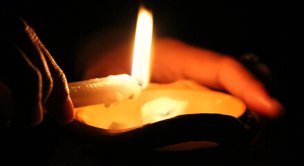 Hands holding a burning candle to drop the wax in the dark