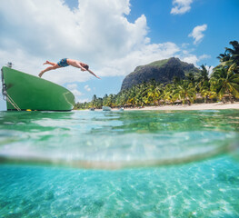 Jumping teenage boy from wooden boat snorkeling in clean turquoise lagoon on Le Morne palm trees beach with Le Morne Brabant mount. Mauritius island. Exotic traveling and vacation concept. © Soloviova Liudmyla