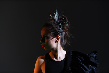 Studio portrait of beautiful young brunette woman in black dress with a crown on her head