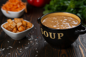 Vegetable cream soup in a black ceramic bowl on a dark wooden background