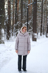 A young woman stands against a background of fir trees under a snowy forest in winter. A girl in a...