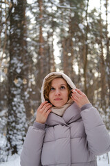 A young woman stands against a background of fir trees under a snowy forest in winter. A girl in a...