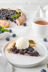 Blueberry galette, open pie or tart with ice cream and cup of tea on a white wooden table. Summer sweet pie.