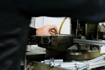 Mann mit schwarzem Pullover sägt Aluminiumstangen an Fräsmaschine in Werkstatt 