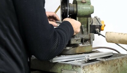 Arbeiter mit schwarzem Pullover beim Sägen von Aluminium vor alter Maschine in Werkstatt - obrazy, fototapety, plakaty