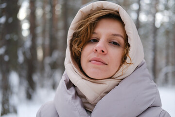 A young woman stands against a background of fir trees under a snowy forest in winter. A girl in a...