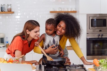 Happy Two asian women lgbtq lesbian and son making salad while preparing food in the kitchen having fun, mother and son cooking activity concept.