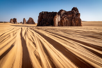 Landscape of Erg Admer in the Sahara desert, Algeria. The tracks of numerous jeeps converge towards the rock formations of the La Vache Qui Pleure site.