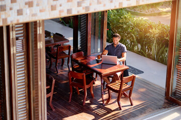 Freelance concept. Young  bearded man working on laptop computer while sitting on cafe terrace.