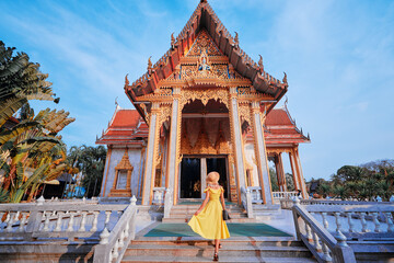 Travel by Asia . Young woman in hat and yellow dress walking near the Chalong buddhist temple on...
