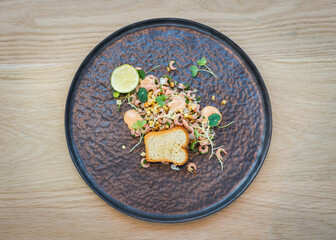 Top view of shrimp salad on black plate on wooden table in restaurant