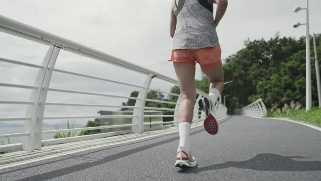 rear view of young asian woman running outdoors on road in park