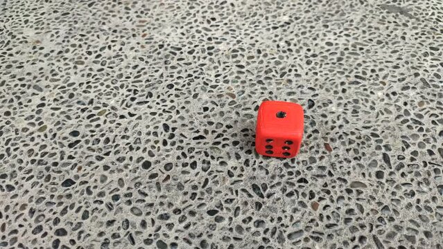 red dice rolled across the stone floor. shows the number one on the top side and the number six on the side.