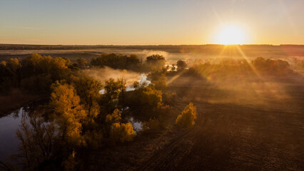 Golden dawn in autumn fog from the lake stretches across the field
