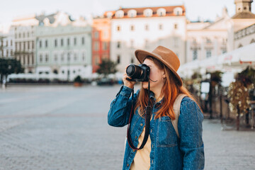 Happy young European tourist with backpack in hat makes photo or video on camera on Market Square in Krakow. Traveling Europe in summer. Vacation concept