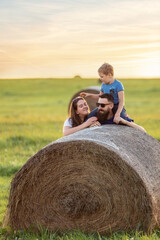 Naklejka na ściany i meble Portrait of a happy close-knit family in a summer meadow near a hay roll