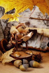 An acorn gnome reads a book while sitting on a stump under a sunny golden autumn leaf. There are...