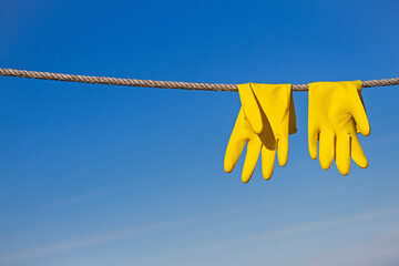 Yellow rubber protective gloves for work or cleaning hang on a rope and dry in the sun beams...