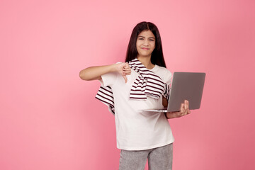 Young upset teenage girl and laptop shows thumb down on pink background in studio.