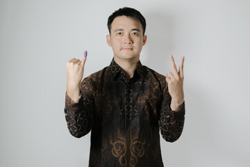 Asian man wearing Indonesian traditional Batik cloth is showing his little finger with purple ink applied to choose number two after Pemilu or Indonesian presidential election on white background