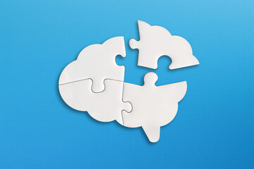 Brain shaped white jigsaw puzzle on blue background. Missing piece of the brain puzzle. Mental...