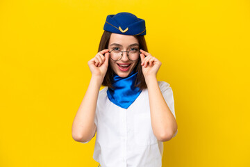 Airplane stewardess Ukrainian woman isolated on yellow background with glasses and surprised