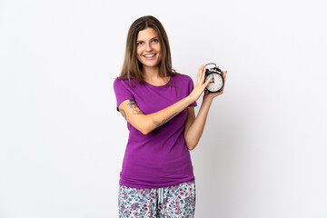 Young slovak woman isolated on white background in pajamas and holding clock with happy expression