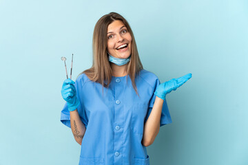 Slovak dentist holding tools isolated on blue background with shocked facial expression