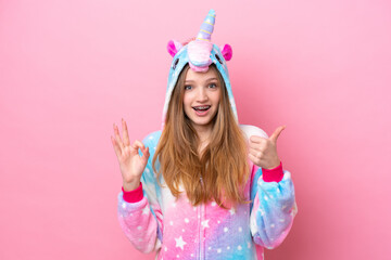 Teenager Russian girl with unicorn pajamas isolated on pink background showing ok sign and thumb up...