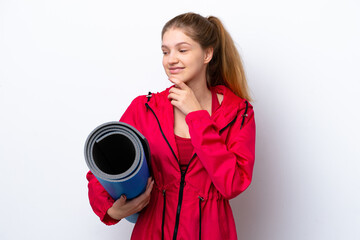 Teenager girl going to yoga classes while holding a mat isolated on white bakcground looking to the...