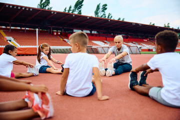 Group of kids and their sports teacher warming up at stadium.