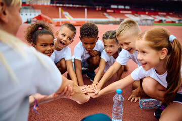 Multiracial group of kids and their sports teacher gathering hands in unity.