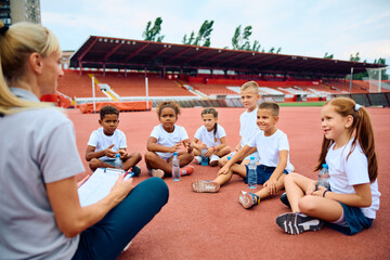 Group of children listening their PE teacher during sports training at stadium.