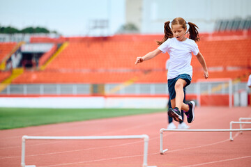 Obraz premium Small girl hurdling on sports training at athletics club.