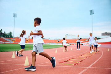 Fototapeta premium Black kid and his friends having PE class at stadium.