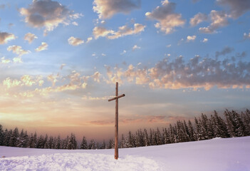 winter snowy fir trees on mountainside on overcast sky background and wooden cross in front...