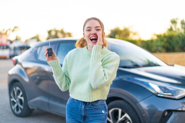 Young pretty girl holding car keys at outdoors shouting with mouth wide open