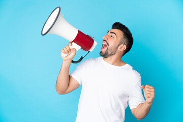 Caucasian man over isolated blue background shouting through a megaphone to announce something in...