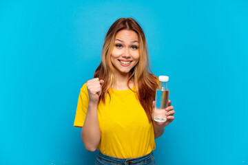 Teenager girl with a bottle of water over isolated blue background celebrating a victory in winner...