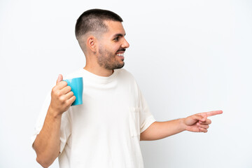 Young caucasian man holding cup of coffee isolated white background pointing to the side to present a product